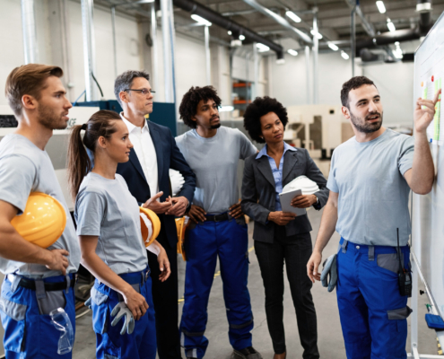 Happy manual worker presenting the results of business development while giving presentation to company leaders and his team in a factory.