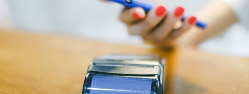 Mão segurando smartphone próximo a uma maquininha de pagamento, representando transação bancária relacionada ao golpe da portabilidade salarial